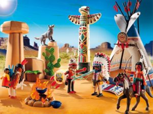 An image of a Playmobil playset that includes a tipi, a totem pole, horses, a coyote, and people dressed in a mishmash of tribal styles in a desert setting.